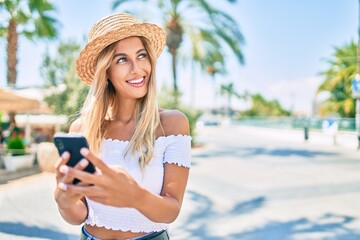 Fototapeta premium Young blonde tourist girl smiling happy using smartphone at the city.