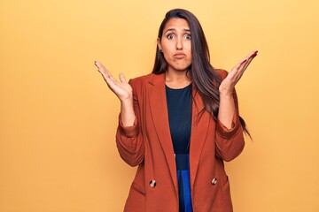 Young beautiful brunette woman wearing elegant jacket clueless and confused with open arms, no idea...