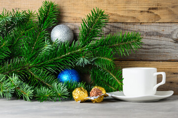 Fir branches with green needles, Christmas balls and a Cup of coffee on a saucer on a wooden background.