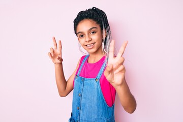 Young african american girl child with braids wearing casual clothes over pink background smiling looking to the camera showing fingers doing victory sign. number two.