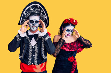 Young couple wearing mexican day of the dead costume over background with hand on head, headache because stress. suffering migraine.