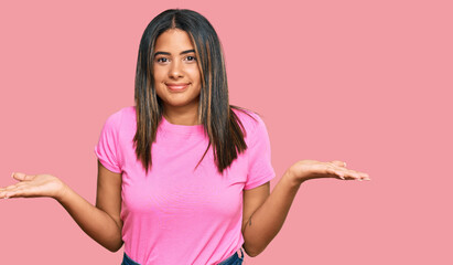 Young latin girl wearing casual clothes clueless and confused expression with arms and hands raised. doubt concept.