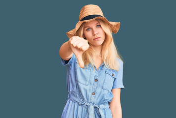 Obraz na płótnie Canvas Young beautiful blonde woman wearing summer hat and dress looking unhappy and angry showing rejection and negative with thumbs down gesture. bad expression.