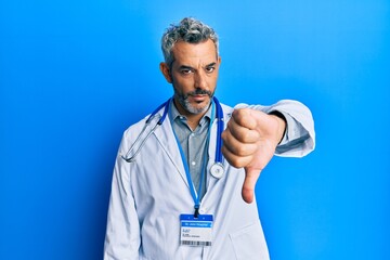 Middle age grey-haired man wearing doctor uniform and stethoscope looking unhappy and angry showing rejection and negative with thumbs down gesture. bad expression.