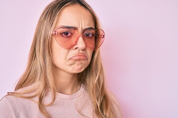 Young beautiful blonde woman wearing heart shaped sunglasses depressed and worry for distress, crying angry and afraid. sad expression.