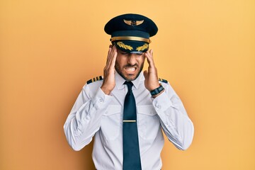 Handsome hispanic man wearing airplane pilot uniform with hand on head, headache because stress. suffering migraine.