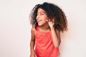 Fototapeta na wymiar African american child with curly hair wearing casual clothes smiling with hand over ear listening and hearing to rumor or gossip. deafness concept.