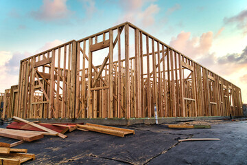 New construction house framing of residential home in California with beautiful blue and pink sunset sky filled with clouds and lumber laying around the construction site property - obrazy, fototapety, plakaty