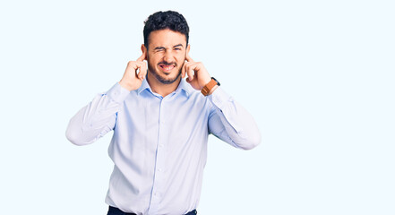 Young hispanic man wearing business clothes covering ears with fingers with annoyed expression for the noise of loud music. deaf concept.