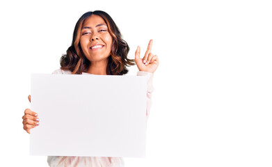Young beautiful mixed race woman holding cardboard banner with blank space surprised with an idea or question pointing finger with happy face, number one