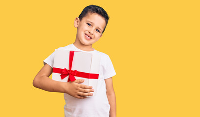 Little cute boy kid holding gift looking positive and happy standing and smiling with a confident smile showing teeth