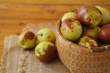 The fresh chinese jujube in bamboo basket on the sackcloth with rough wooden background. Chinese date (Ziziphus mauritiana). Selective focus.  
