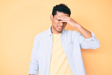Young handsome hispanic man standing over yellow background surprised with hand on head for mistake, remember error. forgot, bad memory concept.