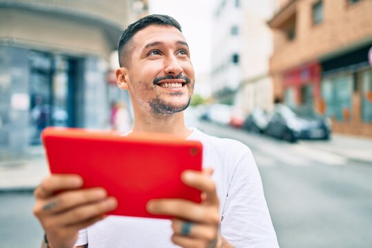 Young hispanic man using touchpad walking at street of city.