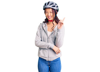 Young beautiful chinese girl wearing bike helmet smiling happy pointing with hand and finger to the side