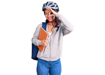 Young beautiful chinese girl wearing student backpack and bike helmet holding book smiling happy doing ok sign with hand on eye looking through fingers