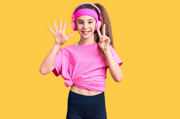 Obraz na płótnie Canvas Cute hispanic child girl wearing gym clothes and using headphones showing and pointing up with fingers number seven while smiling confident and happy.