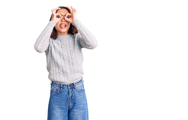 Young beautiful chinese girl wearing casual clothes doing ok gesture like binoculars sticking tongue out, eyes looking through fingers. crazy expression.