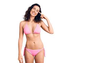 Young beautiful hispanic woman wearing bikini smiling pointing to head with one finger, great idea or thought, good memory