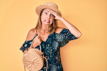 Middle age hispanic woman wearing summer hat holding wicker bag stressed and frustrated with hand on head, surprised and angry face