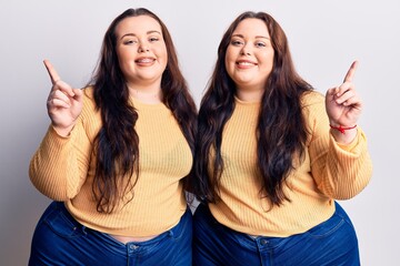 Young plus size twins wearing casual clothes smiling confident pointing with fingers to different directions. copy space for advertisement