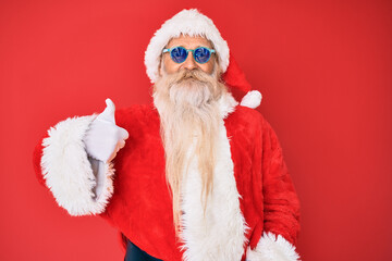 Old senior man wearing santa claus costume and sunglasses smiling happy and positive, thumb up doing excellent and approval sign