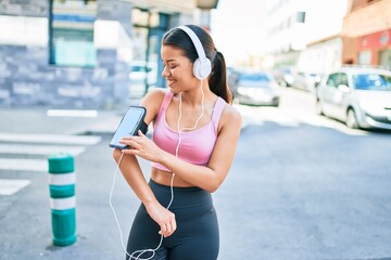 Young beautiful hispanic sport woman wearing runner outfit and headphones, listening to music wearing device on arm band
