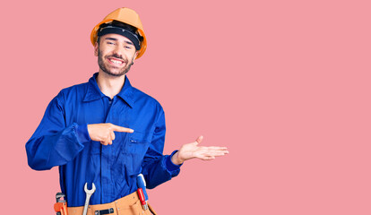 Young hispanic man wearing worker uniform amazed and smiling to the camera while presenting with hand and pointing with finger.