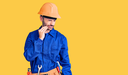 Young hispanic man wearing worker uniform touching mouth with hand with painful expression because of toothache or dental illness on teeth. dentist