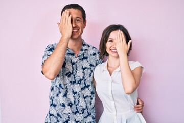 Beautiful couple wearing casual clothes covering one eye with hand, confident smile on face and surprise emotion.