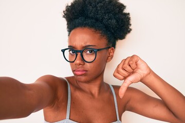 Young african american woman wearing casual clothes and glasses making selfie by the camera with angry face, negative sign showing dislike with thumbs down, rejection concept