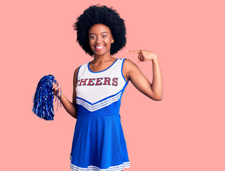 Young african american woman wearing cheerleader uniform holding pompom looking confident with...