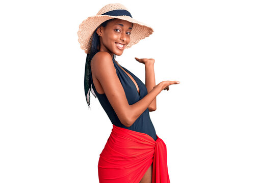 Young african american woman wearing swimsuit and summer hat inviting to enter smiling natural with open hand