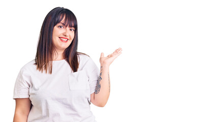 Young plus size woman wearing casual clothes smiling cheerful presenting and pointing with palm of hand looking at the camera.