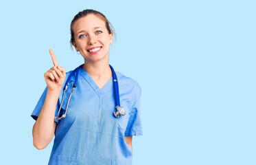 Young beautiful blonde woman wearing doctor uniform and stethoscope showing and pointing up with...