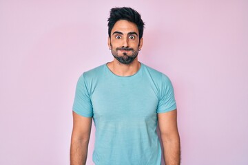 Handsome hispanic man with beard wearing casual clothes puffing cheeks with funny face. mouth inflated with air, crazy expression.