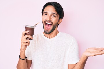 Handsome hispanic man drinking mate infusion celebrating achievement with happy smile and winner expression with raised hand