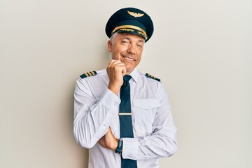 Handsome middle age mature man wearing airplane pilot uniform looking confident at the camera smiling with crossed arms and hand raised on chin. thinking positive.