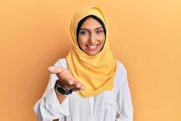 Young brunette arab woman wearing traditional islamic hijab scarf smiling cheerful offering palm...