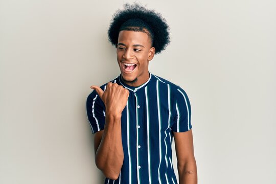 African american man with afro hair wearing casual clothes pointing thumb up to the side smiling happy with open mouth