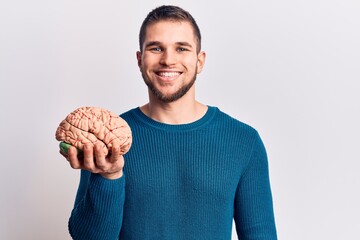 Young handsome man holding brain looking positive and happy standing and smiling with a confident...
