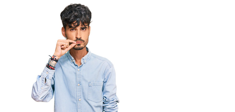 Young hispanic man wearing casual clothes mouth and lips shut as zip with fingers. secret and silent, taboo talking
