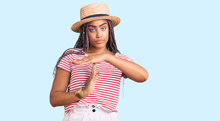 Obraz na płótnie Canvas Young african american woman with braids wearing summer hat doing time out gesture with hands, frustrated and serious face