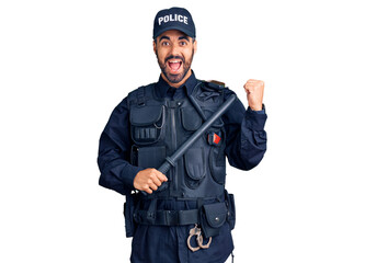 Young hispanic man wearing police uniform holding baton screaming proud, celebrating victory and success very excited with raised arms