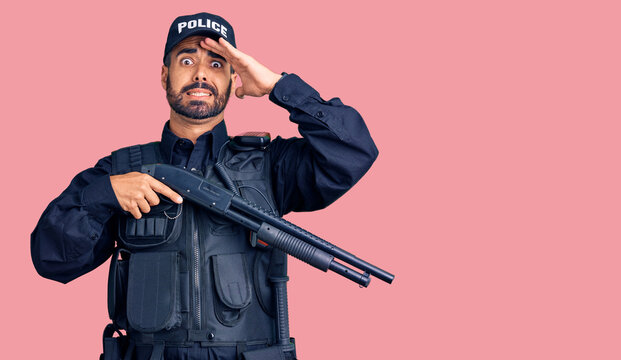 Young hispanic man wearing police uniform holding shotgun stressed and frustrated with hand on head, surprised and angry face