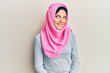 Young caucasian woman wearing traditional islamic hijab scarf looking away to side with smile on face, natural expression. laughing confident.