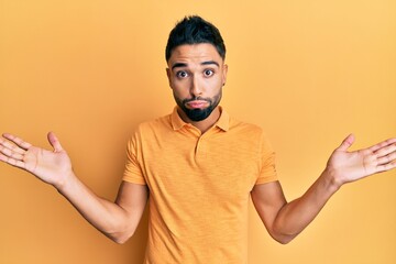 Young man with beard wearing casual clothes clueless and confused with open arms, no idea and...