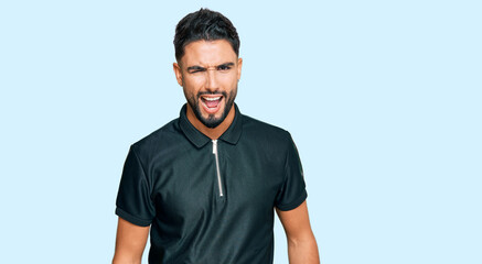 Young man with beard wearing sportswear winking looking at the camera with sexy expression,...