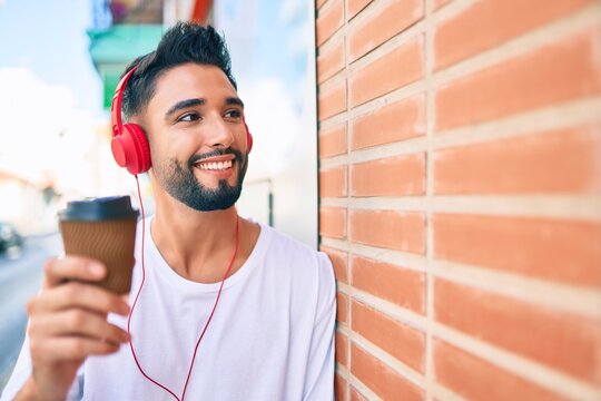 Young Arab Man Drinking Take Away Coffee And Using Headphones At The City.