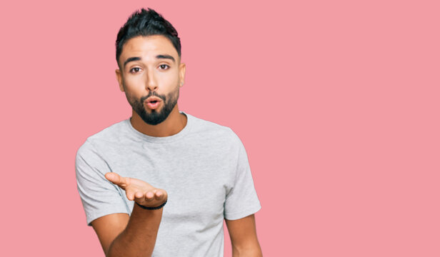 Young man with beard wearing casual grey tshirt looking at the camera blowing a kiss with hand on air being lovely and sexy. love expression.